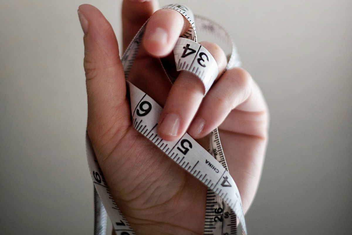 A hand wrapping a white and yellow tape measure around a wrist