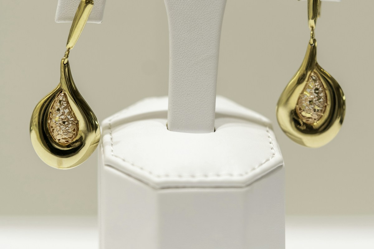 A pair of gold drop earrings hanging on a white display stand