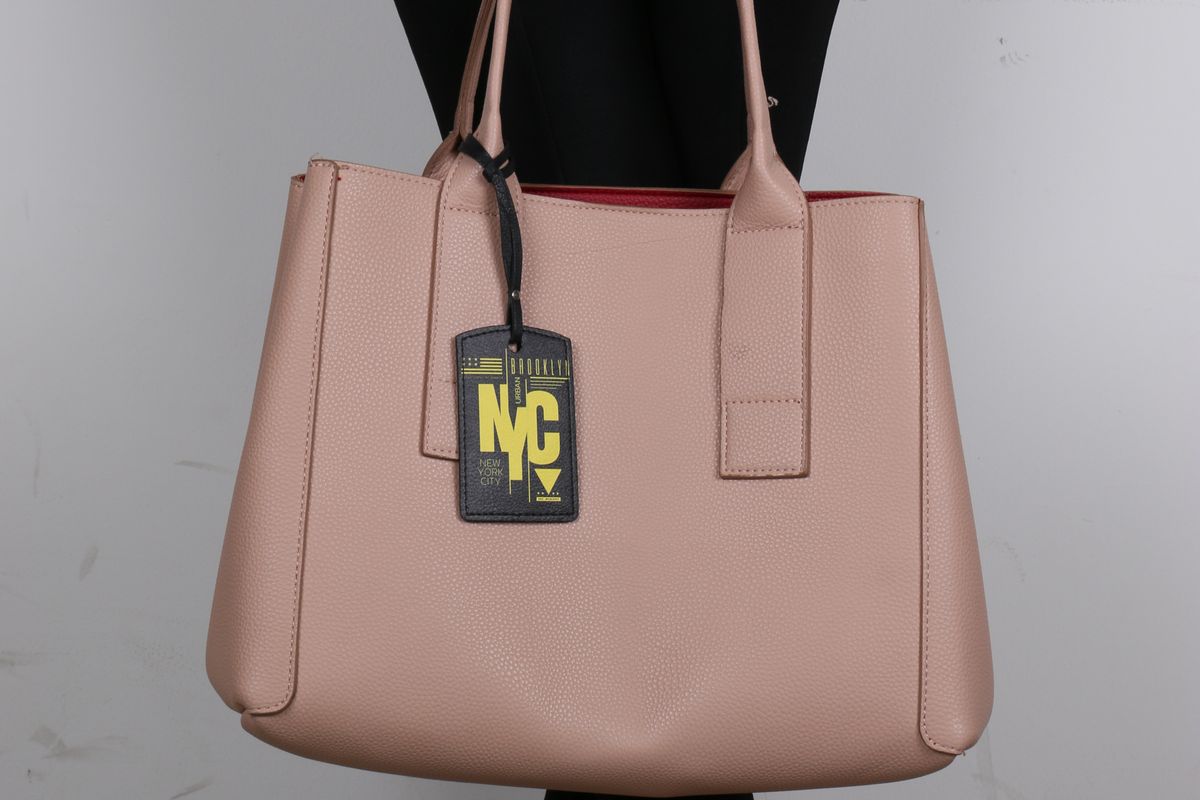 A person holding a blush leather tote bag by its top handles