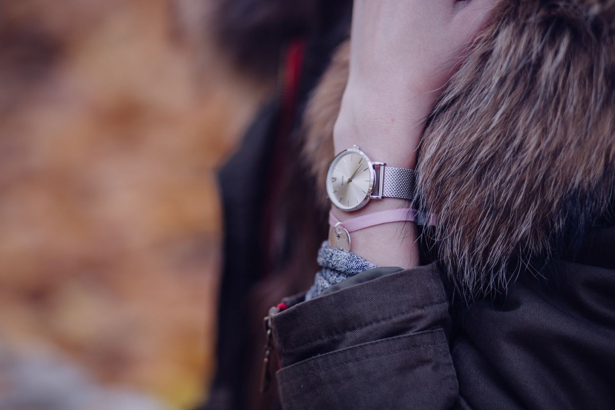 A round gold-dial watch on a mesh bracelet strap worn on a wrist under a winter coat