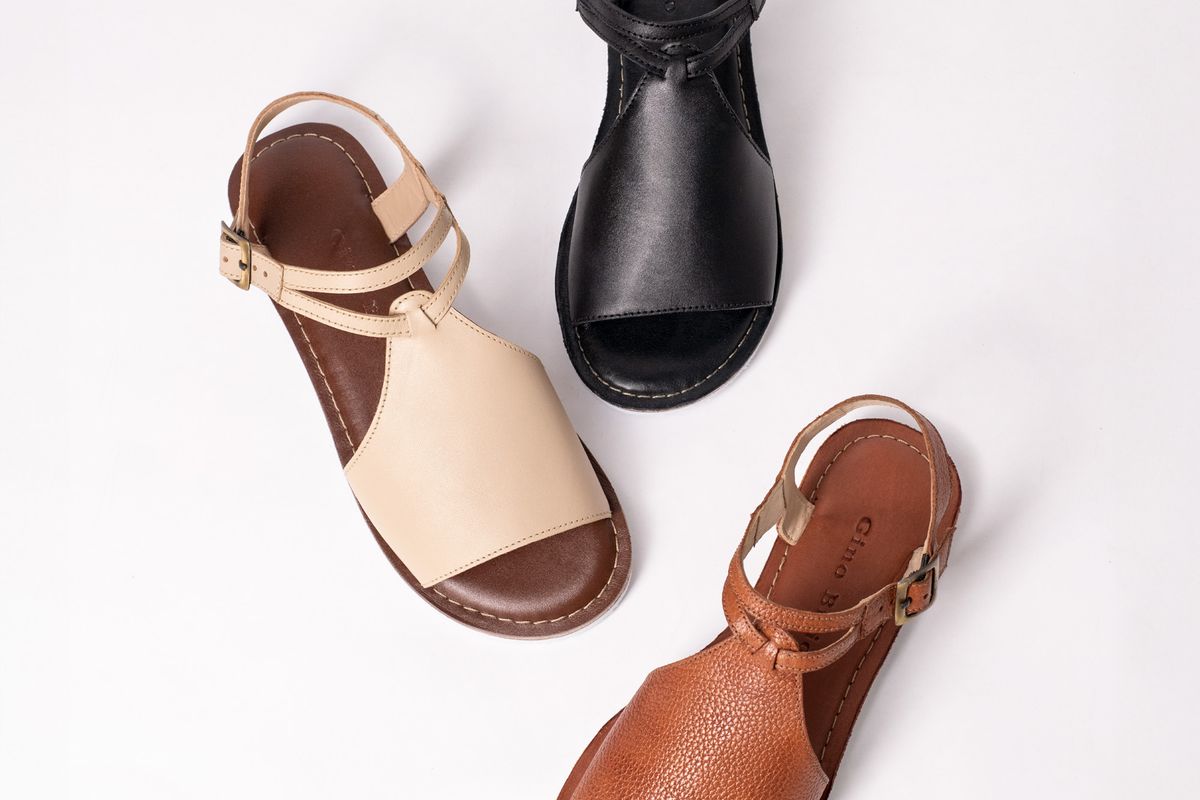 A pair of two-strap leather sandals with a contoured cork footbed lying on a wooden surface
