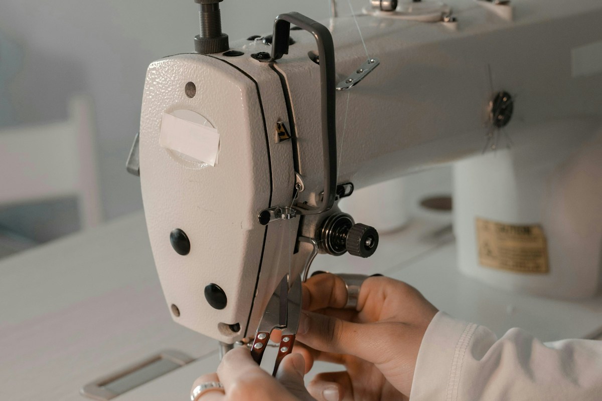 Hands guiding fabric through a white sewing machine in a bright workroom