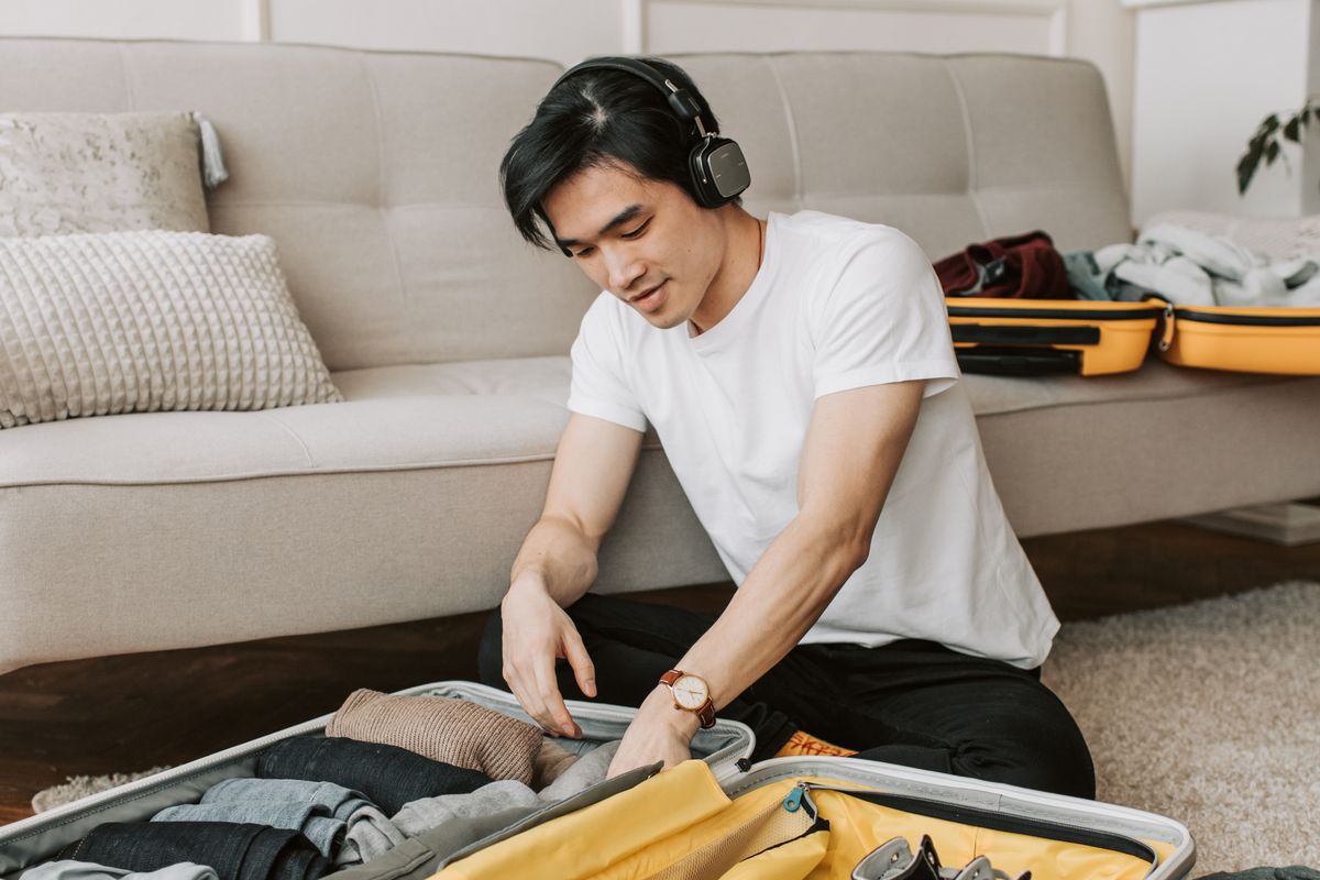 A man packing clothes into a bag while wearing headphones